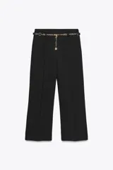 Pantalón tobillero negro de tiro alto con cinturón de cadena dorada. Presenta falsos bolsillos con solapa en la espalda, pernera recta y cierre lateral con cremallera oculta.
