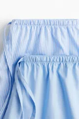 Shorts de pijama celestes con cintura elástica y cordón ajustable. Uno de los lados es de tela a rayas verticales blancas y celestes.