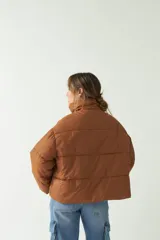 Campera puffer color marrón con cuello alto, corte cropped a la cadera, cierre metálico y botones.