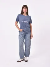 Remera blanca de algodón con cuello redondo y manga corta. Presenta un pequeño bordado en el pecho izquierdo con una figura que parece ser una persona acostada en una tabla de surf o flotador.