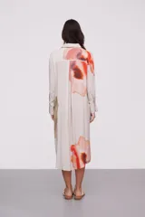 Vestido camisero midi color beige con estampado abstracto en tonos naranja, rojo, verde y amarillo. Tiene cuello camisero, mangas largas con puños abotonados y cierre frontal con botones.