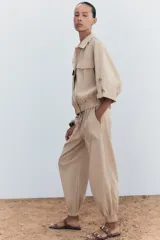 Pantalón de tiro medio color beige, con cintura elástica ajustable con cordones, bolsillos delanteros y puños elásticos en los tobillos.