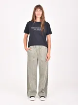 Remera blanca de manga corta con cuello redondo y un estampado artístico en tonos rojo oscuro y negro que simula una figura femenina con pantalón ancho a rayas.