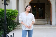 Blusa blanca de manga larga con elástico en puños, escote en pico y cierre frontal con botones. Detalles de bordados con hilado en tonalidad camel y acabado con entredoses a tono.