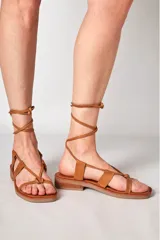 Sandalia de cuero color marrón con tiras finas y cordones para atar al tobillo.