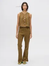 Pantalón de denim color marrón, de tiro alto y corte oxford con aberturas laterales. Presenta apliques metálicos alrededor de los bolsillos delanteros y traseros, y a lo largo de la parte externa del pantalón.