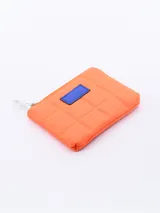 Monedero cuadrado acolchado color naranja con cierre superior y parche azul.