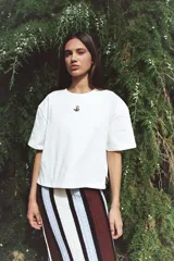 Remera blanca de algodón con manga corta y cuello redondo. Presenta un pequeño bordado de una flor en el pecho.