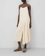 Vestido midi color crema con breteles finos, escote en V y corte asimétrico. Presenta una sección lisa y otra con bordado calado.