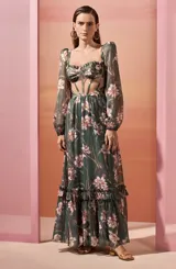 Vestido largo de gasa con estampado floral en tonos verdes y rosas. Presenta un corpiño estructurado con cut-outs y mangas largas transparentes. La falda es amplia con volantes en el ruedo.