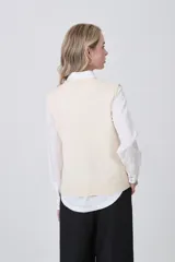 Chaleco de punto color crema, con cuello en V, cierre frontal de botones y dos bolsillos frontales.