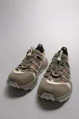 Zapatilla deportiva color beige con aberturas laterales, ajuste de cordones y suela de goma.