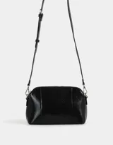 Bandolera negra de cuerina con doble compartimento con cierre y charm lateral. Tiene correa regulable y desmontable.
