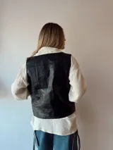 Chaleco negro de cuero con botones metálicos y bolsillos delanteros.