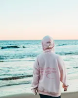 Buzo hoodie rosa con capucha y cordones ajustables. Estampado en la espalda con el texto "ClassyWaves Surf Company" y un logo de una ola.