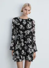 Vestido corto negro con estampado floral blanco, de mangas largas acampanadas, cuello redondo, lazo en la cintura y volados en el ruedo.