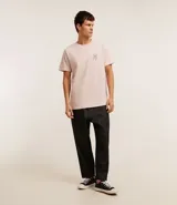 Remera de algodón color rosa claro, de corte clásico, con cuello redondo y manga corta. Presenta un pequeño estampado de un timón en el pecho y un estampado con letras en la espalda.