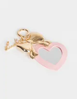 Llavero con dije de espejo en forma de corazón con borde rosa, moño dorado y dije con la palabra "Lucky".