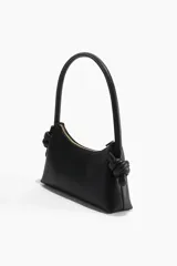 Bolso de hombro pequeño color negro, con cierre superior y asa rígida con nudos decorativos en los extremos. Forro de tafeta.