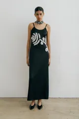 Vestido largo negro de breteles finos, con escote redondo y detalle de apliques florales blancos en el frente.