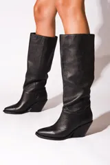 Bota de caña alta color negro, confeccionada en cuero vacuno. Tiene punta fina, taco de 6.5cm y suela de caucho antideslizante.