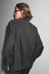 Camisa negra de lyocell con cuello redondo, manga larga con puños y bajo asimétrico con aberturas laterales. Cierre frontal con botones.