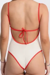 Malla de una pieza color crudo con textura gofrada y ribetes de contraste en color rojo en el escote, tirantes y contorno de pierna.