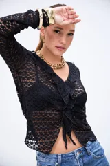 Blusa negra de encaje con diseño calado, escote en V, volados en el frente y cierre con lazos. De manga larga y corte ajustado.