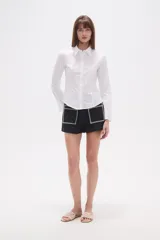 Camisa blanca de algodón, entallada, con cuello camisa y cierre frontal de botones. Presenta mangas largas con puños sencillos.