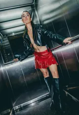 Minifalda roja de cuero sintético con volados y apliques metálicos circulares.