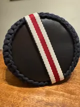 Bolso tejido a crochet con hilo de trapillo en colores negro, blanco y rojo. Tiene base de cuero vegano y correa de tela ajustable con detalles en rojo y blanco.