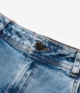 Pantalón de jean azul claro, modelo flare, con cintura elástica, trabillas para cinturón, bolsillos delanteros y traseros, y botón en forma de flor.