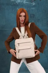 Mochila mediana de símil cuero color beige, con asa superior, dos compartimentos principales con cierre y dos bolsillos frontales con cierre. Las correas son ajustables y de color beige.