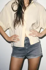 Shorts de jean de algodón, tiro alto, color azul claro desgastado. Presenta cinco bolsillos, cierre frontal con botón metálico y bajo desflecado con vuelta.