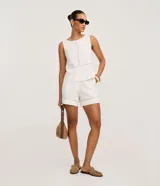 Short femenino confeccionado en viscolino de color blanco, con cierre tradicional, trabillas en la cintura y bolsillos. Presenta un detalle decorativo de entremeio calado en el bajo.