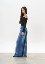 Pantalón de jean de tiro medio, corte wide leg, color azul con costuras verticales blancas en el frente.