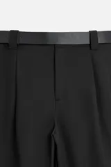 Pantalón negro de corte recto con cinturón de cuero sintético, pliegues frontales, bolsillos laterales y traseros con solapa.