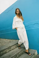 Camisa blanca de manga corta con cuello solapa, bolsillos frontales con tapeta, bajo con elástico y cierre frontal con botones a presión.