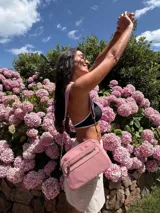 Bandolera color rosa viejo con detalles en cuero marrón claro, múltiples cremalleras metálicas y herrajes plateados. Incluye correa ancha ajustable con el logo de la marca.