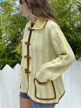 Cárdigan de punto color amarillo manteca con rayas verticales en crudo. Tiene cuello polo, cierre frontal con botones de soga y bolsillos de parche.