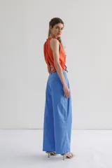 Top sin mangas color naranja con abertura en el delantero y espalda. Detalle de fruncido en el cuello y ruedo que se ajusta y cierra con lazo en contraste color azul.