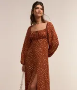 Vestido midi color ladrillo con estampado floral blanco, escote cuadrado con lazo ajustable, mangas largas abullonadas y abertura lateral en la falda.