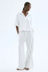 Camisa blanca de lino y viscosa, de corte holgado, con cuello clásico, botones frontales, mangas cortas y bajo redondeado.