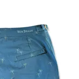 Short de baño azul con estampado de palmeras, pretina fija con hebillas metálicas laterales, botón a presión y cierre frontal. Incluye tres bolsillos (dos laterales y uno trasero). Confeccionado en tela con 10% spandex de secado rápido y mesh hipoalergénico en el interior.
