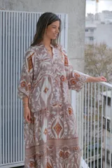 Vestido largo color rosa con estampado floral y geométrico en tonos blanco y naranja. Tiene cuello mao, mangas 3/4 y corte escalonado en la falda.