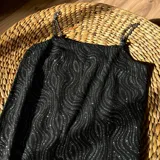 Vestido corto negro con estampado de líneas onduladas plateadas y tirantes de cadena metálica.