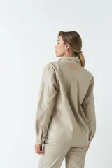 Sobrecamisa color beige de efecto cuero, con cuello clásico, cierre frontal con botones a tono, mangas largas con puños abotonados, dos bolsillos con solapa en el pecho y corte recto.