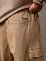 Pantalón cargo color beige de algodón orgánico elástico, con cintura elástica y corte recto. Presenta bolsillos laterales, traseros y tipo cargo en las piernas.