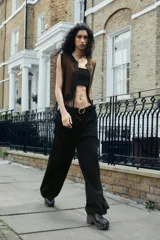 Pantalón ancho color beige, de tiro alto con pinzas delanteras, cinturón negro con hebilla dorada, bolsillos frontales y falsos bolsillos de doble vivo en la espalda.