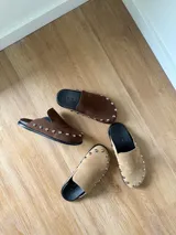 Zuecos color beige con tachas plateadas, base negra y plantilla con el logo de la marca.